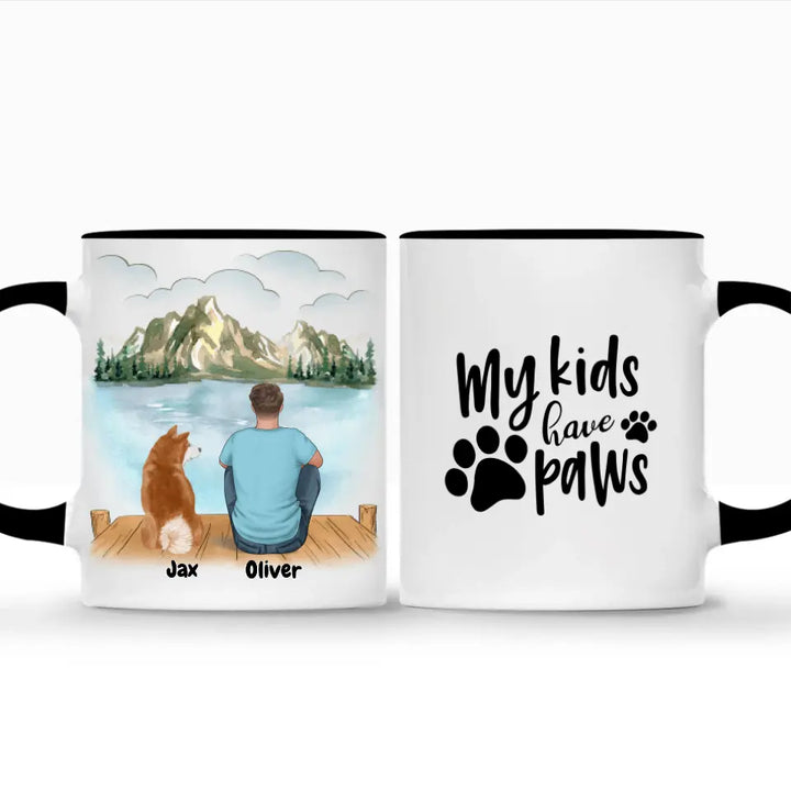 Custom pet and owner coffee mug set with black handles and rims, featuring a personalized illustration of a man and his dog sitting by a scenic lake with names "Jax" and "Oliver" below. The second mug displays the quote "My kids have paws" with paw print graphics. Perfect gift for pet lovers, dog owners, and personalized keepsakes. Dishwasher & microwave safe. Order now!